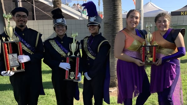 Schüler der Bell High School in bunten Kostümen halten vor einem Festival mit Zelten und Palmen ihre Trophäen.