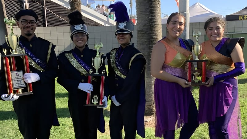 Schüler der Bell High School in bunten Kostümen halten vor einem Festival mit Zelten und Palmen ihre Trophäen.