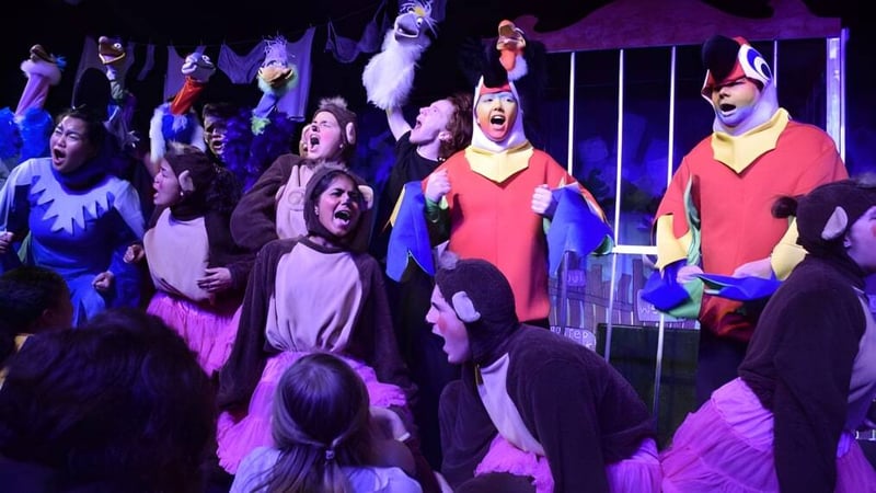 Schüler des Belmont City College führen ein Theaterstück auf einer Bühne mit dramatischer Beleuchtung auf.