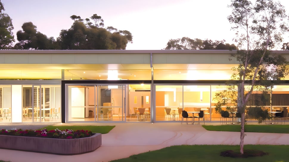 Das moderne, verglaste Gebäude des Belmont City College mit Grünfläche und Bepflanzung im Vordergrund.