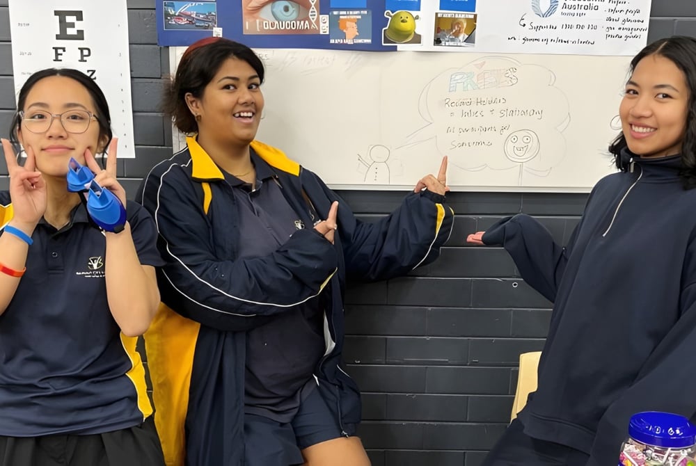 Drei Schülerinnen in Schuluniformen stehen vor einer Tafel im Unterricht am Belmont City College.