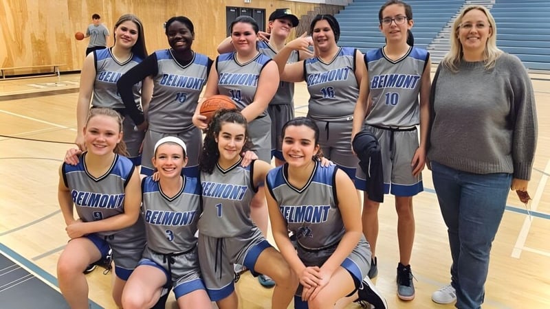 Gruppe von Schülerinnen der Belmont Secondary School in Basketballuniformen in einer Sporthalle.