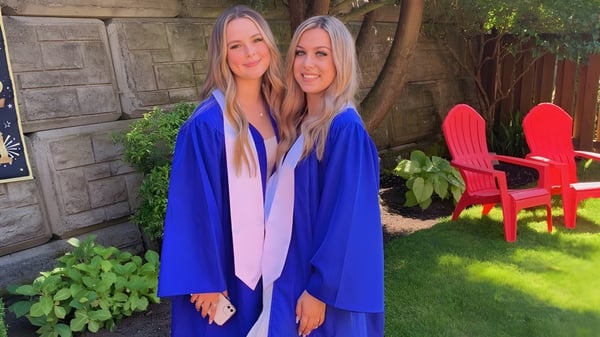 Zwei Schülerinnen mit langen blonden Haaren stehen zusammen im Garten der Belmont Secondary School vor grüner Vegetation und einem roten Adirondack-Stuhl.