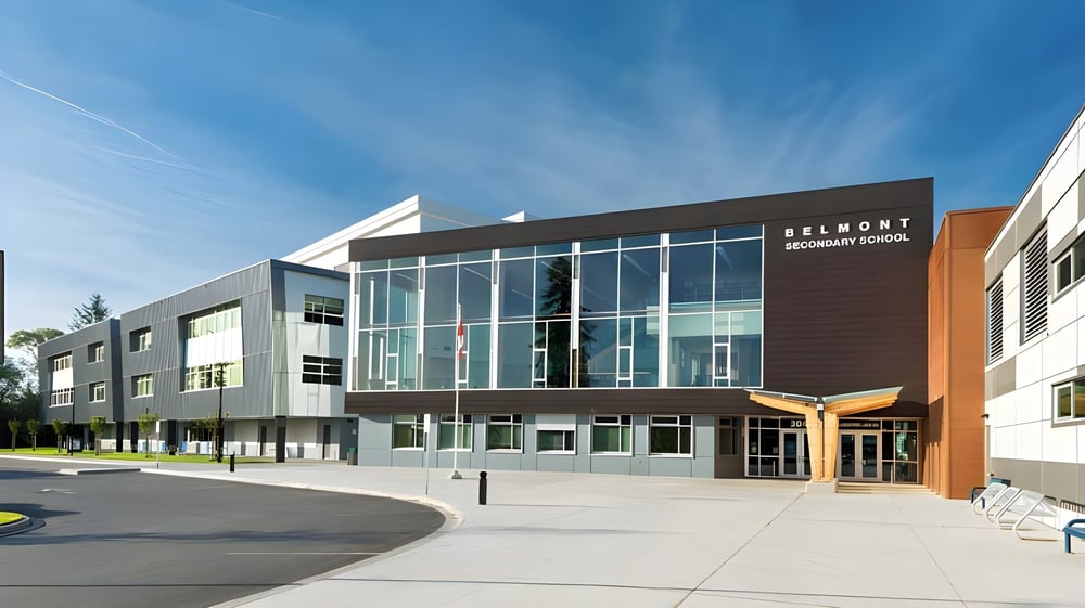 Das moderne mehrstöckige Gebäude mit Glasfassade der Belmont Secondary School ist von einem gepflasterten Bereich und Begrünung umgeben.