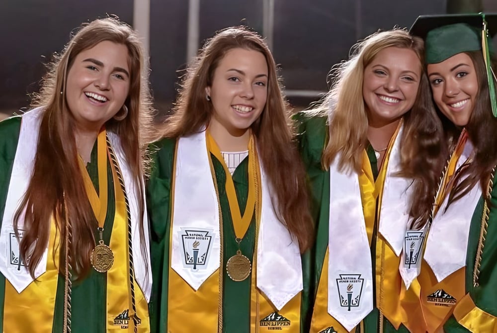 Vier Schülerinnen der Ben Lippen School posieren in Abschlusskleidung vor dunklem Hintergrund.