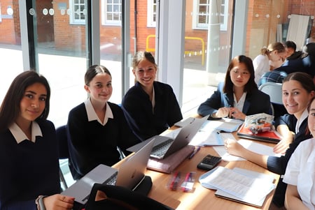 Eine Gruppe von Schülerinnen der Benenden School sitzt in formeller Kleidung an einem Tisch im Klassenraum.