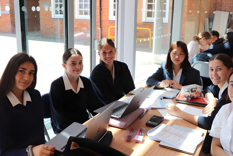 Eine Gruppe von Schülerinnen der Benenden School sitzt in formeller Kleidung an einem Tisch im Klassenraum.