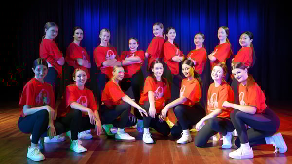 Eine Gruppe junger Schülerinnen sitzt auf der Bühne der Benowa State High School vor einem blauen Vorhang.