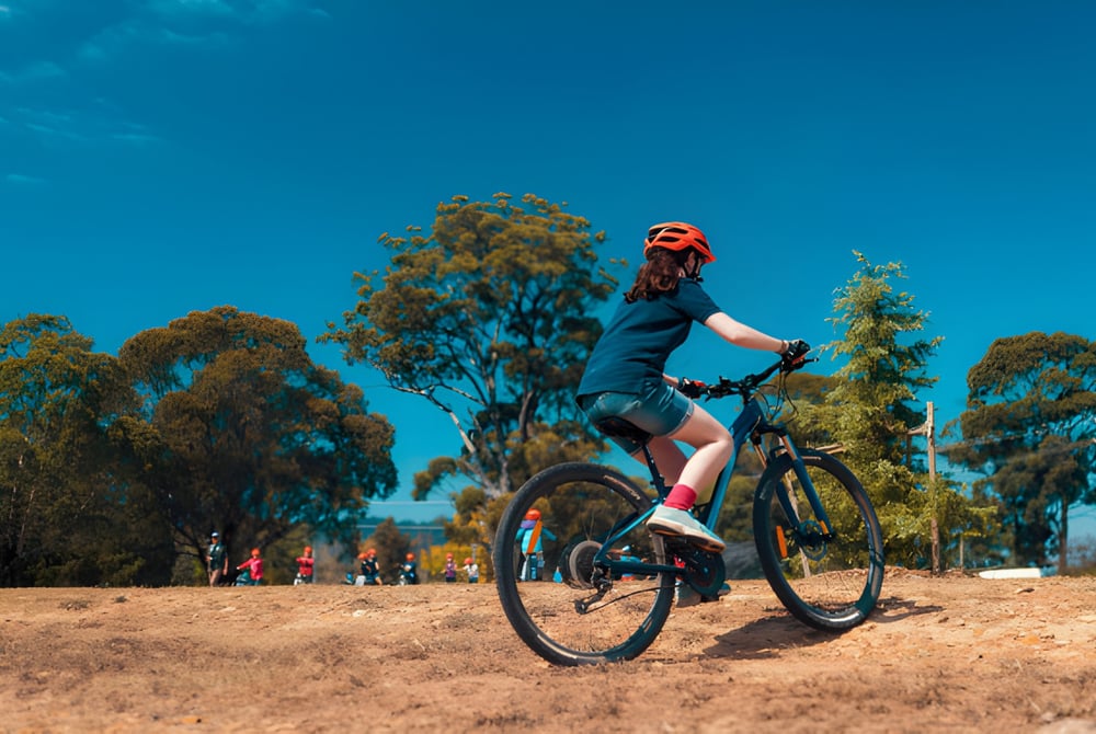 Eine Person in Sportkleidung fährt mit dem Fahrrad auf einem Weg umgeben von Bäumen auf dem Gelände der Benowa State High School.