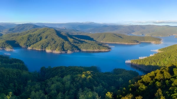 Eine Luftaufnahme zeigt eine ruhige Seelandschaft mit Wald und Bergen in der Nähe der Benowa State High School.