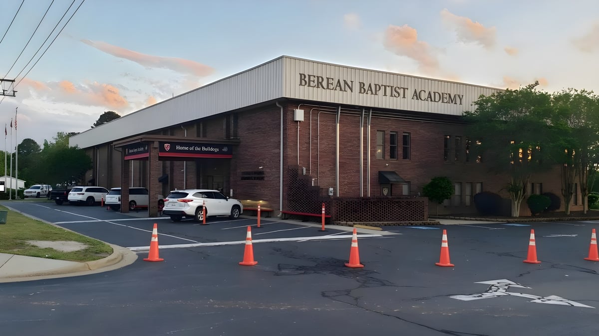 Das Backsteingebäude der Berean Baptist Academy ist von einem Parkplatz mit Fahrzeugen und Absperrungen umgeben.