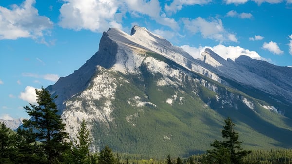 Majestätische schneebedeckte Berge mit blauem Himmel und grünem Wald vor der Bernice McNaughton High School.
