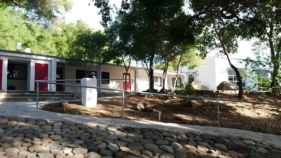 Das moderne Schulgebäude der Besant Hill School ist von Bäumen umgeben und zeigt einen Weg zum Eingang sowie einen Steingarten im Vordergrund.