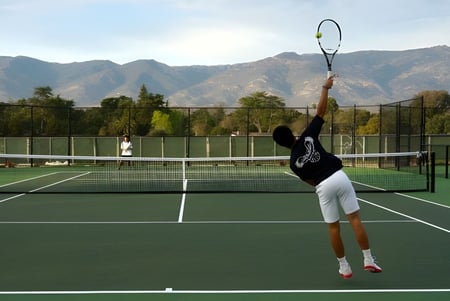 Eine Person in Sportkleidung spielt Tennis auf dem Tennisplatz der Besant Hill School mit Bergen und Grün im Hintergrund.