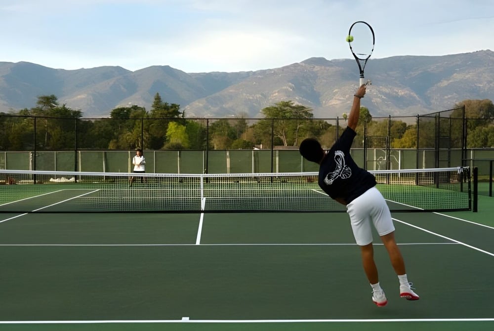 Eine Person spielt Tennis auf dem gepflegten Tennisplatz der Besant Hill School vor grünem Bergpanorama.