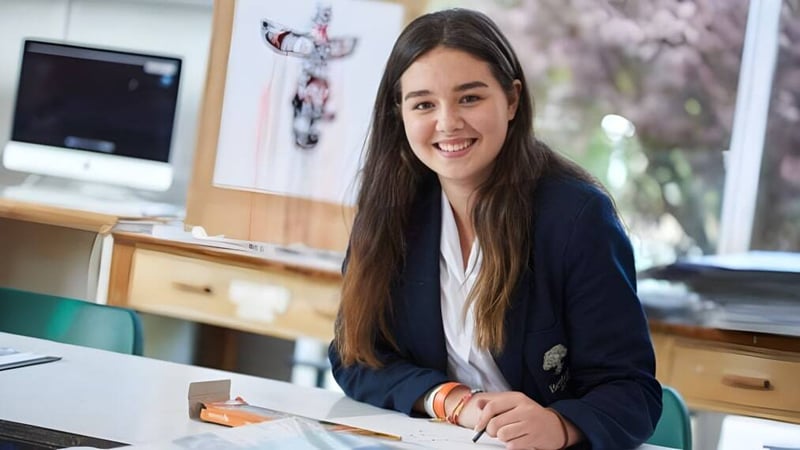 Eine Schülerin sitzt lächelnd an ihrem Schreibtisch im Klassenraum der Bethany School.