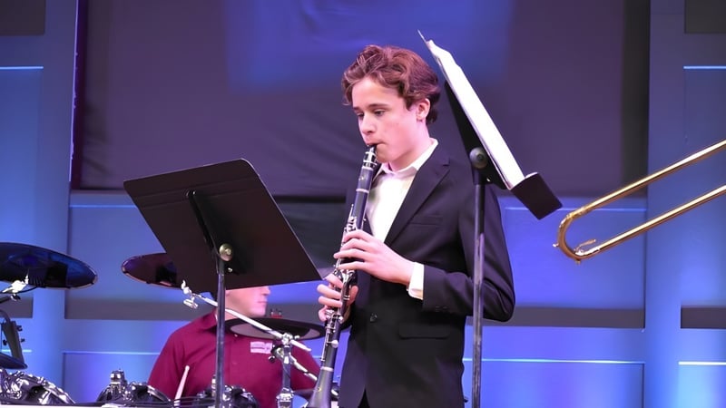 Eine Person in Anzug spielt ein Musikinstrument auf der Bühne der Bethel Christian Schools mit blau beleuchtetem Hintergrund.