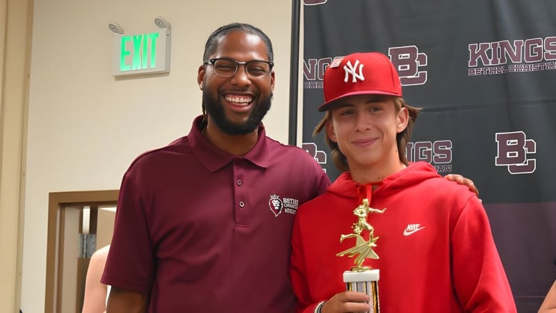 Ein Mann mit Bart und ein Junge mit rotem Hut posieren gemeinsam bei einer Sportveranstaltung auf dem Campus der Bethel Christian Schools.