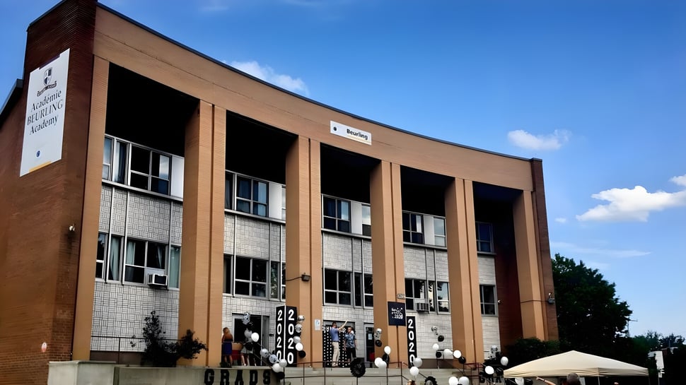 Das mehrstöckige Backsteingebäude mit großen Fenstern und geschwungener Fassade der Beurling Academy steht vor klarem Himmel.