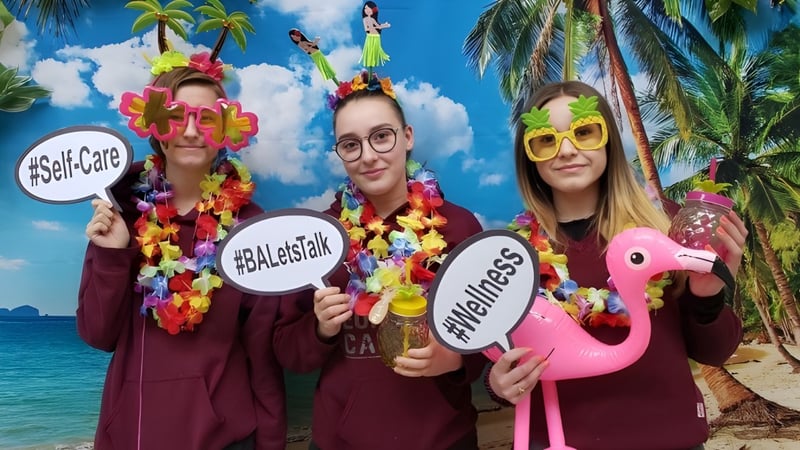 Drei Schülerinnen und Schüler der Beurling Academy tragen bunte hawaiianische Outfits vor einer tropischen Strandkulisse.