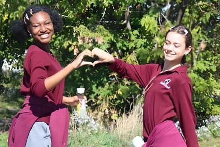 Zwei Schülerinnen der Beurling Academy formen mit ihren Händen draußen ein Herz.