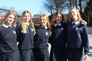 Eine Gruppe von fünf Schülerinnen in Schuluniformen steht vor einem Gebäude auf dem Gelände der Beverly High School.