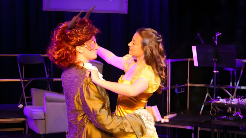 Zwei Personen umarmen sich auf der Bühne mit buntem Licht und Musikequipment am Bexhill College.