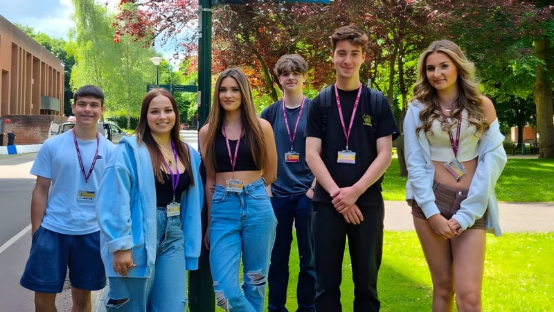 Schüler des Bexhill College stehen gemeinsam in einem parkähnlichen Bereich mit Bäumen und Gebäuden im Hintergrund.