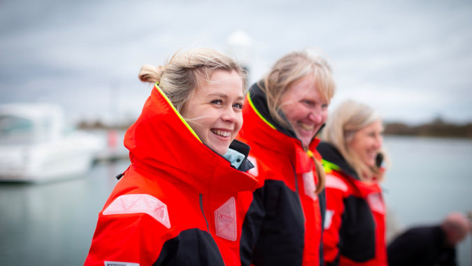 Zwei Personen mit roten Rettungswesten stehen vor einem Gewässer auf dem Campus des Bexhill College.