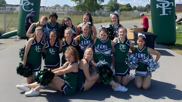 Eine Gruppe Cheerleader der Billings Central Catholic High School posiert im Freien vor einem umzäunten Sportfeld.