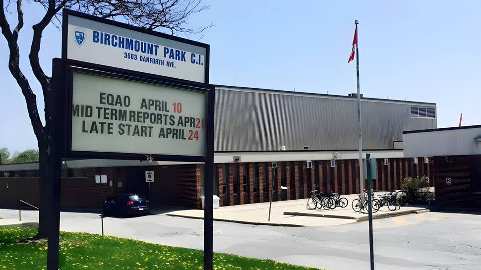 Das Schild des Birchmount Park Collegiate Institute informiert über Zwischenberichte und spätere Unterrichtsbeginnzeiten vor dem Schulgebäude mit Fahrrädern.