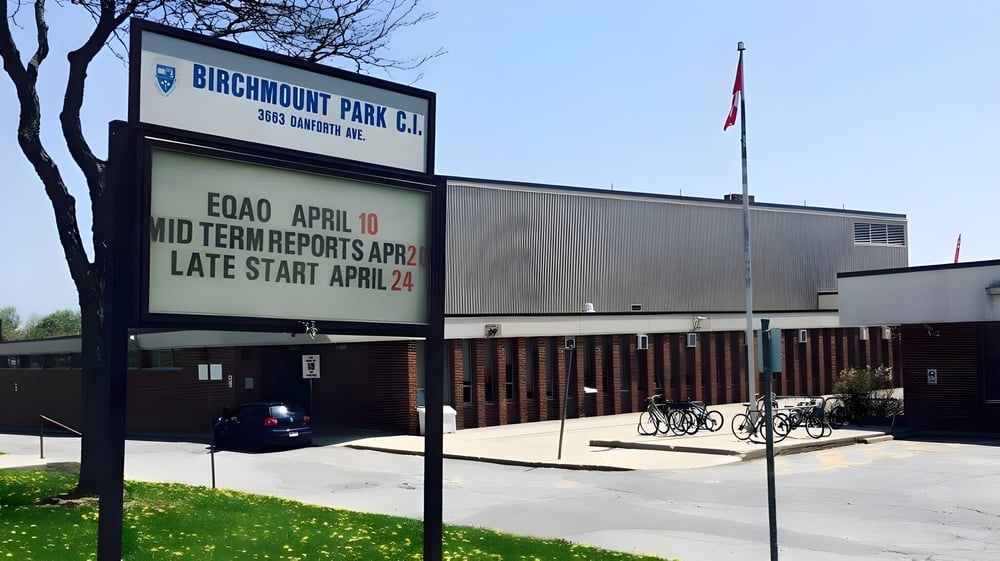 Das Schild des Birchmount Park Collegiate Institute informiert über Zwischenberichte und spätere Unterrichtsbeginnzeiten vor dem Schulgebäude mit Fahrrädern.