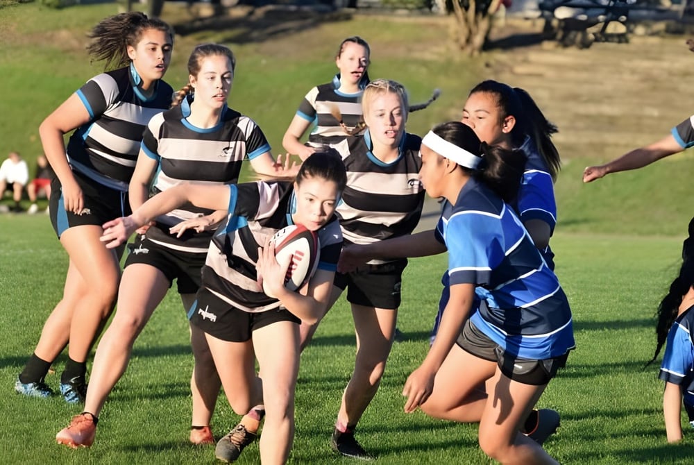 Eine Gruppe Schülerinnen in Sportkleidung steht auf einem Rasenfeld auf dem Campus des Birkenhead College.