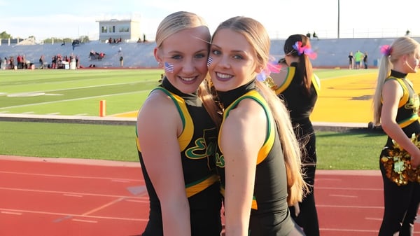 Zwei Cheerleader der Bishop Carroll High School posieren gemeinsam auf dem Sportfeld vor einem Stadion.
