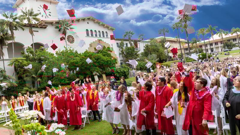 Absolventinnen und Absolventen der Bishop Garcia Diego High School versammeln sich vor einem Gebäude mit Palmen unter blauem Himmel.