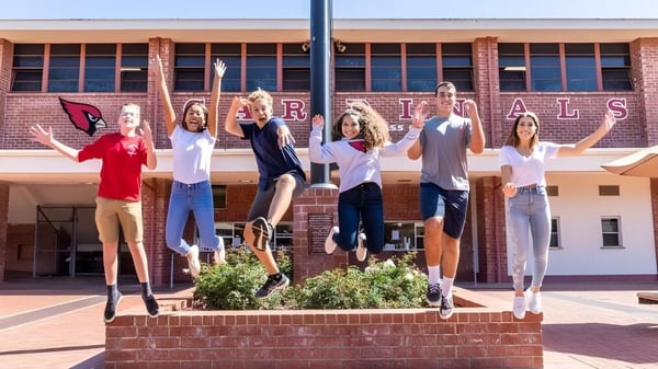 Eine Gruppe Schüler der Bishop Garcia Diego High School steht auf einer Backsteinmauer vor einem Gebäude mit dem Schriftzug Rivals.