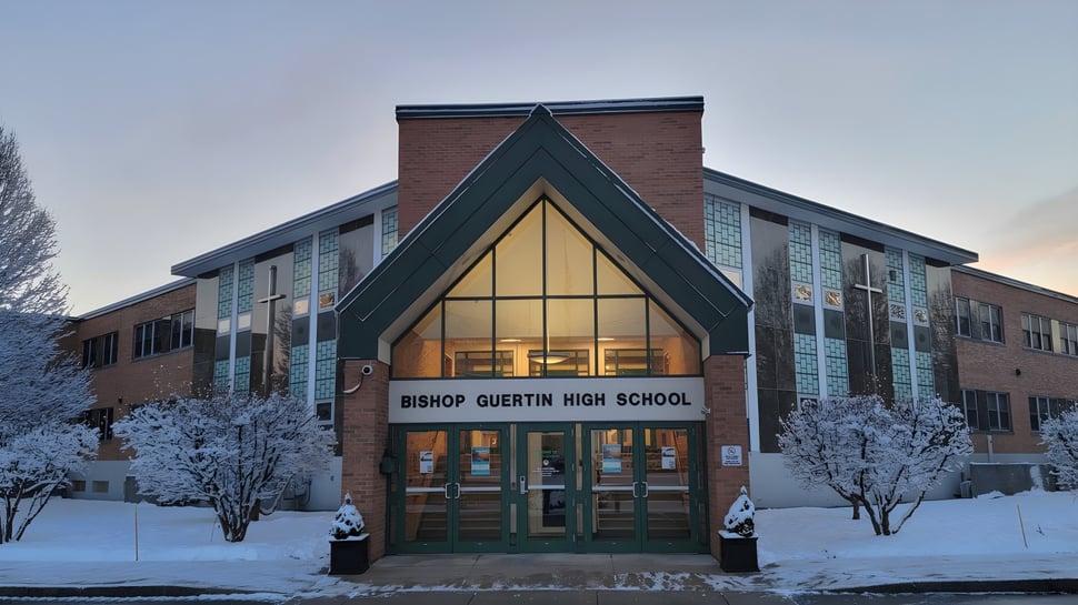 Das Backsteingebäude der Bishop Guertin High School mit Satteldach steht umgeben von schneebedeckten Bäumen.