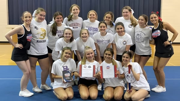 Eine Gruppe junger Athletinnen in Sportuniformen posiert in der Sporthalle der Bishop Guilfoyle Catholic High School.