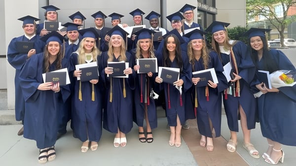 Eine Gruppe von Absolventen der Bishop Heelan Catholic High School steht im Freien in akademischer Kleidung und hält ihre Zeugnisse.