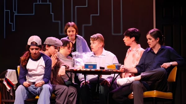 Schüler der Bishop Kearney High School versammeln sich an einem Tisch mit verschiedenen Gegenständen vor geometrischem Hintergrund.