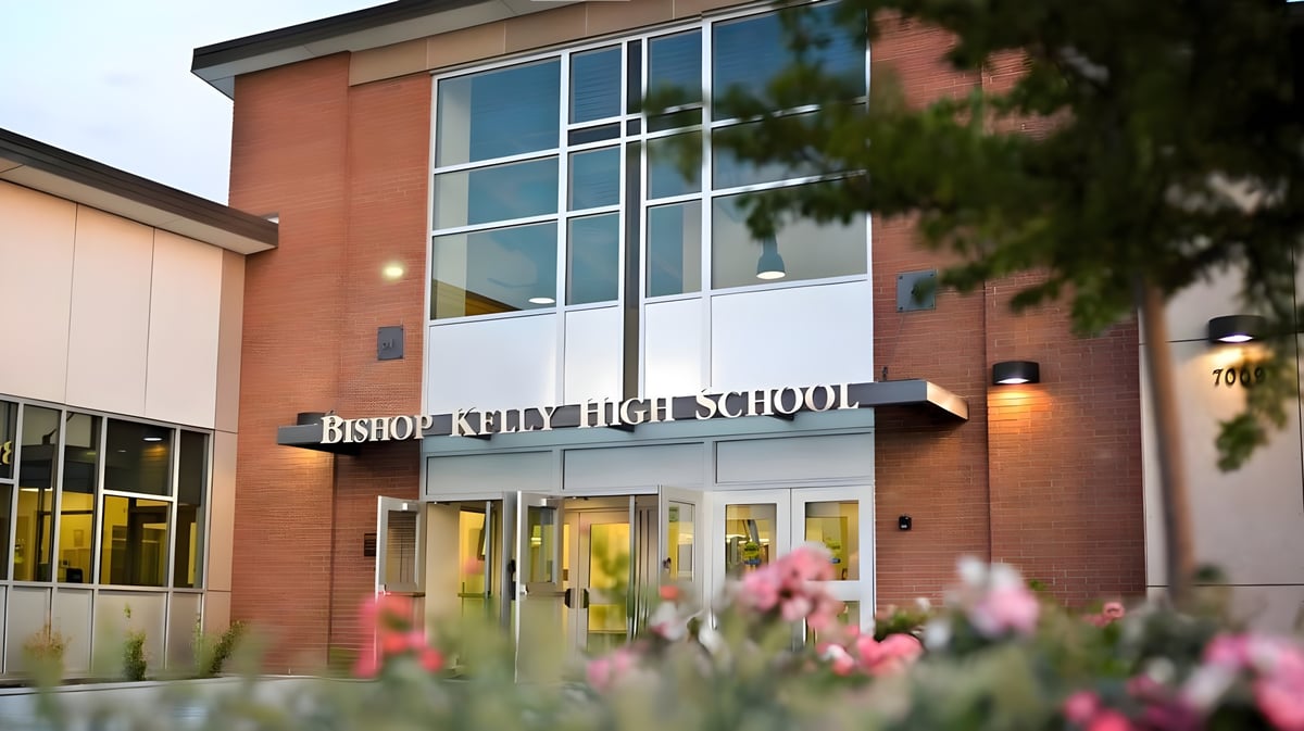 Die Außenansicht des Schulgebäudes von Bishop Kelly High School mit blühenden pinken Blumen im Vordergrund.