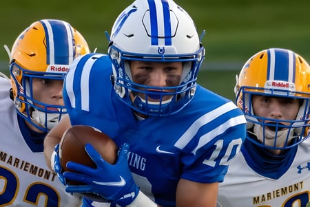 Drei Footballspieler stehen auf dem Spielfeld der Bishop Mahoney High School in blauen und gelben Trikots.