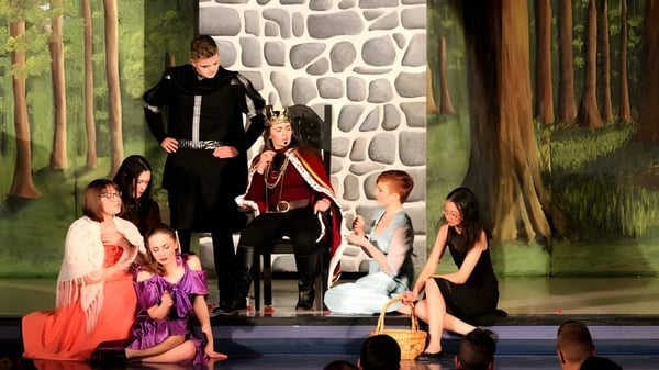 Schüler der Bishop Mahoney High School proben eine Theateraufführung vor einer Steinmauer und Waldkulisse.