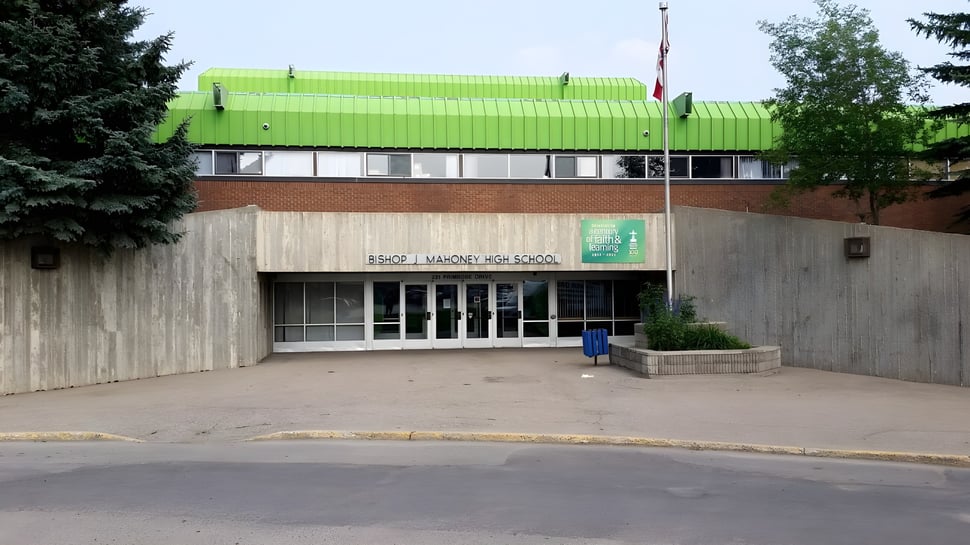 Das gruen bedachte moderne Gebaeude steht auf dem gepflasterten Bereich der Bishop Mahoney High School umgeben von Baeumen und Sträuchern.