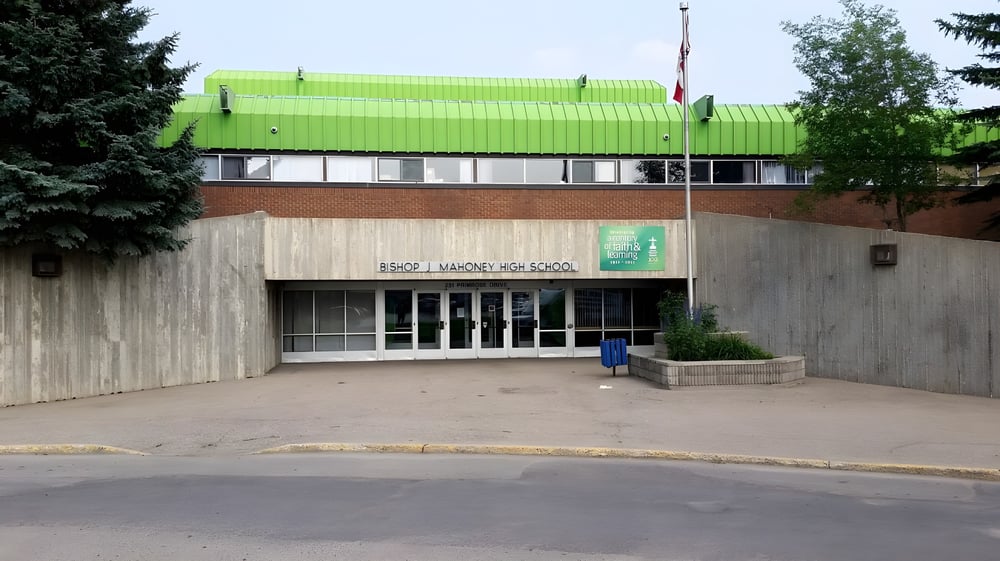 Das gruen bedachte moderne Gebaeude steht auf dem gepflasterten Bereich der Bishop Mahoney High School umgeben von Baeumen und Sträuchern.