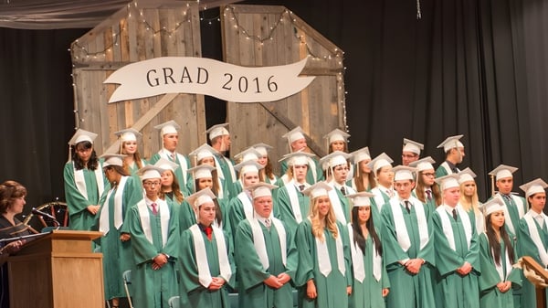 Absolventen der Bishop Mahoney High School stehen in grünen Talaren auf der Bühne vor einem Banner mit der Aufschrift Grad 2016.