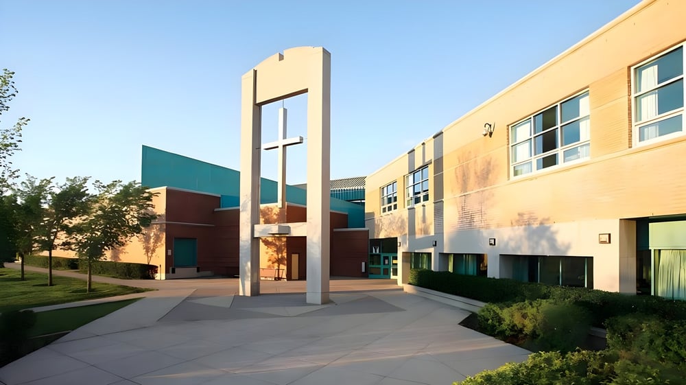 Das moderne mehrfarbige Gebäude der Bishop McNally High School mit hohem Bogeneingang steht vor grüner Umgebung.