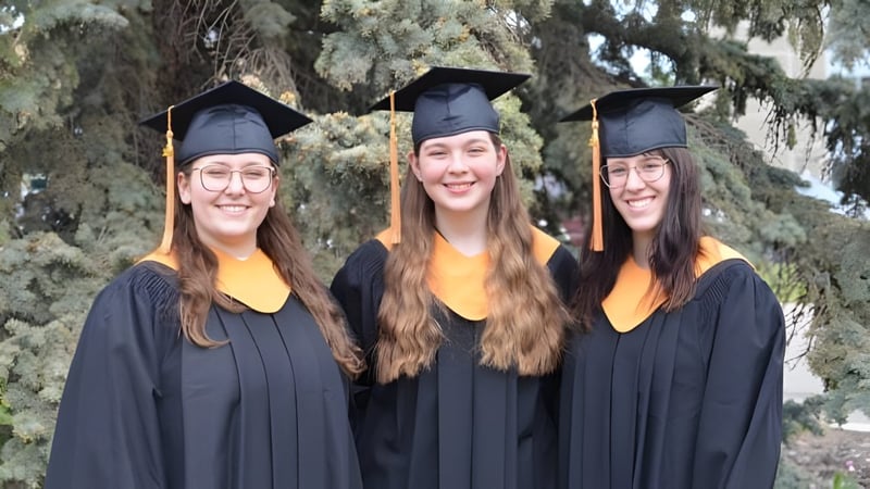 Drei Absolventinnen der Bishop O'Byrne High School stehen gemeinsam im Freien in einer bewaldeten Umgebung.