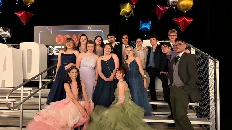 Eine Gruppe von Schülerinnen und Schülern der Bishop O'Byrne High School posiert auf einer Bühne mit bunten Luftballons und Dekorationen im Hintergrund.