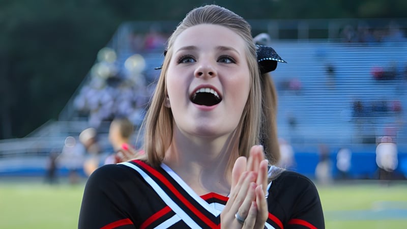 Eine Cheerleaderin der Bishop Rosecrans High School steht mit überraschter Miene auf dem Sportfeld vor Zuschauern.
